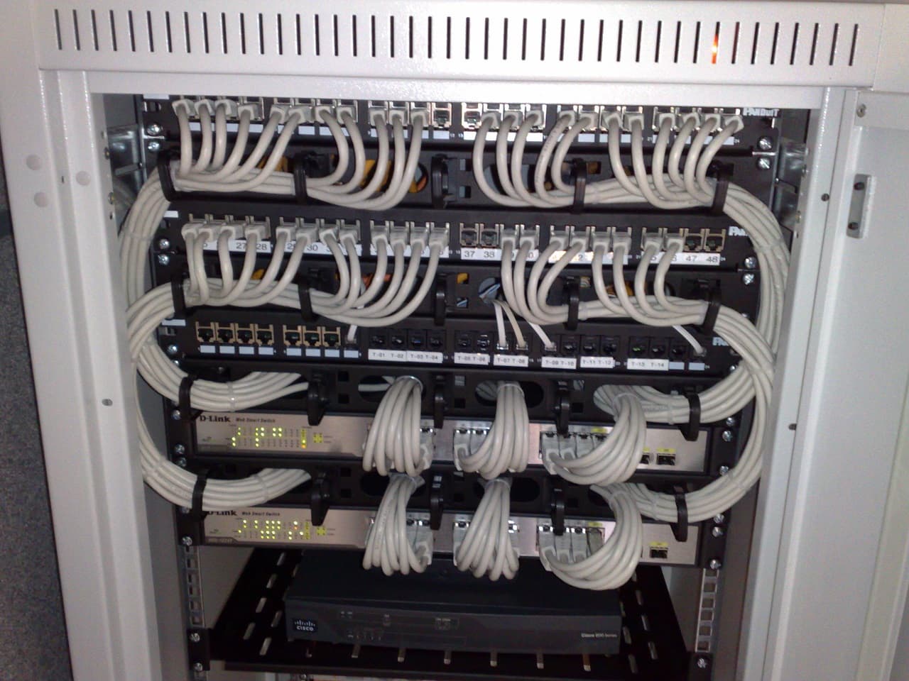 Rack-mounted Ethernet switches connected to patch panels with network cables.